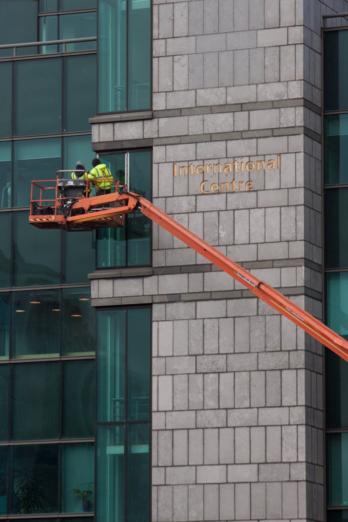 Construction workers on crane repairing building facade at International Centre.